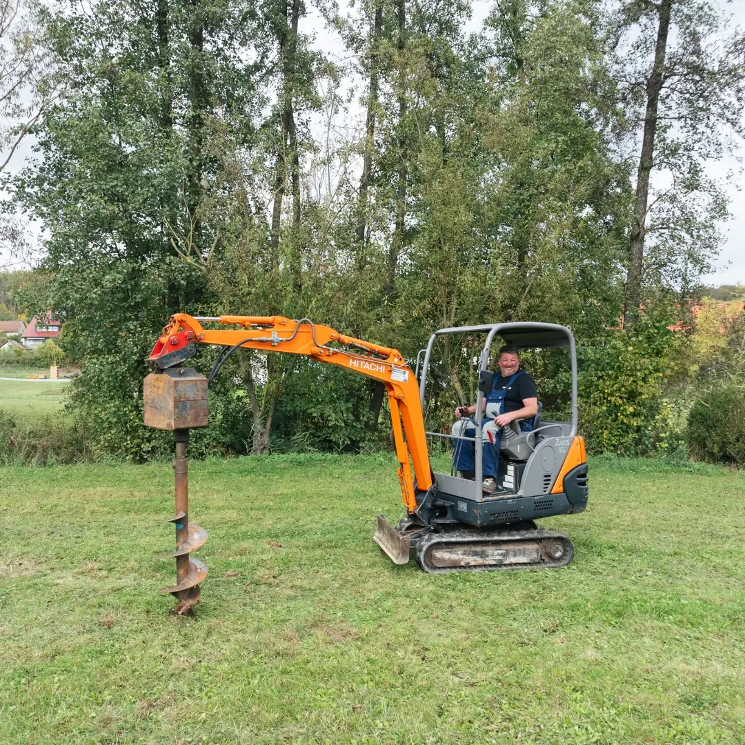 Kleiner Bagger mit Erdbohrer bei Arbeiten auf einer Wiese. Einsatz für präzise Erdarbeiten und Bohrungen in der Region Neustadt an der Aisch.