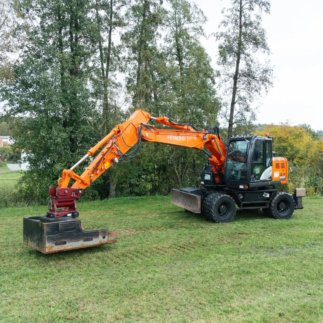 Moderner orangefarbener Bagger bei Forst- und Erdarbeiten auf einer Wiese in ländlicher Umgebung. Einsatz von Spezialmaschinen für professionelle Forstarbeiten in der Region Neustadt an der Aisch.
